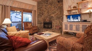 A cozy living room with a stone fireplace, wooden furniture, and a television on a wooden cabinet.