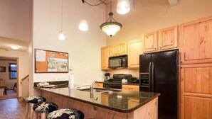 A kitchen with wooden cabinets, a black refrigerator, a microwave, and a large island with bar stools.