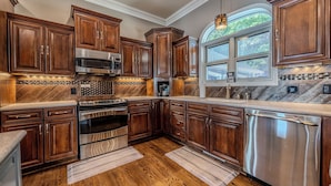 A kitchen with wooden cabinets, stainless steel appliances, and a window with a view of trees. - Upscale Lakefront Luxury at Lake of the Ozarks - Private Dock, Quiet Cove (Lake Ozark)