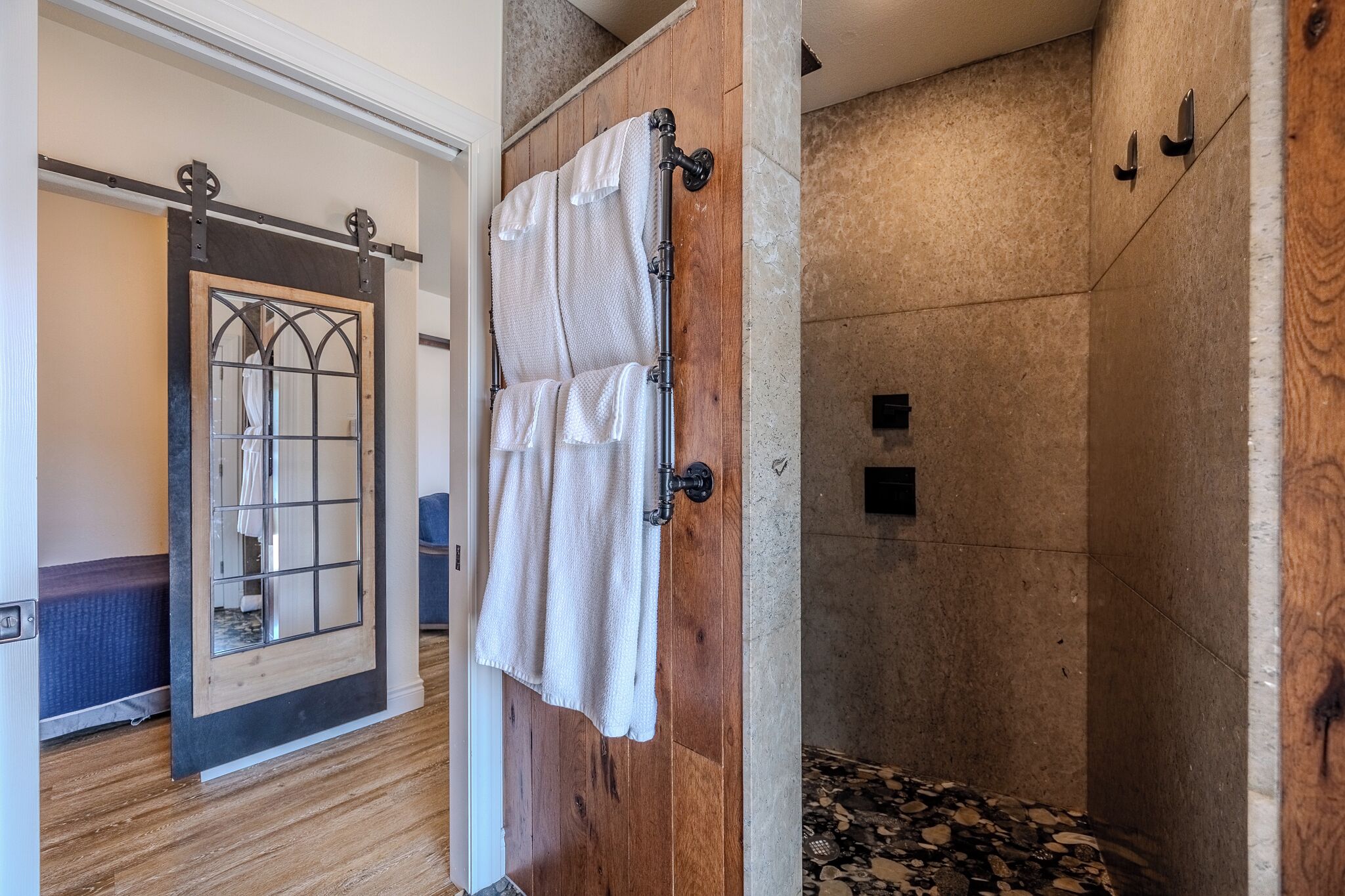 Une porte en bois avec une serviette suspendue à un porte-serviettes, un espace douche avec un sol en pierre et un mur recouvert de panneaux de bois.
