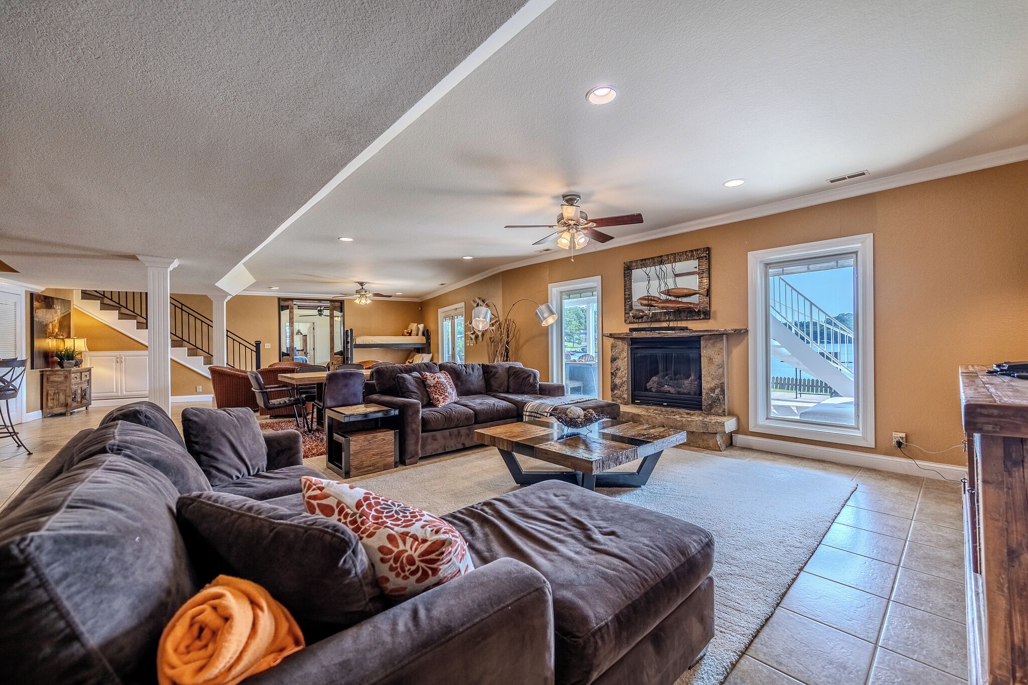 A spacious living room with a fireplace, large windows, and a staircase leading to another level.