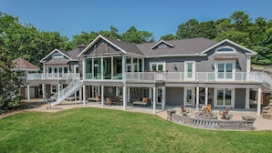 A large, two-story house with multiple balconies, a covered patio, and a fire pit area. - Upscale Lakefront Luxury at Lake of the Ozarks - Private Dock, Quiet Cove (Lake Ozark)