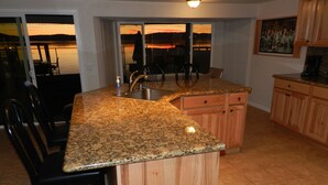 Una cocina con encimeras de granito, armarios de madera, un fregadero y una zona de comedor con sillas.