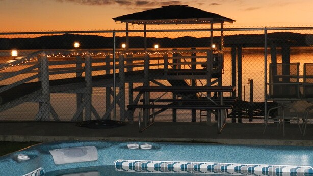 Una piscina con jacuzzis, una terraza de madera y un pabellón con vistas a un cuerpo de agua.