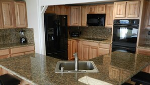 Una cocina con encimeras de granito, electrodomésticos de acero inoxidable, armarios de madera y una isla central con taburetes de bar.