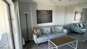 A modern living room with a grey sofa, a coffee table, and a ceiling fan. - Direct Ocean Front Condo With Heated Pool Located Directly on the Ocean (St Augustine)