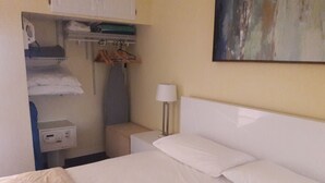 A hotel room with a bed, a bedside table with a lamp, a wardrobe, and a painting on the wall. - Direct Ocean Front Condo With Heated Pool Located Directly on the Ocean (St Augustine)