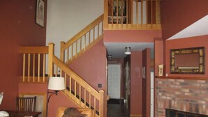 A staircase with wooden railings leading to a second floor, a fireplace with a brick surround, and a lamp on a table.
