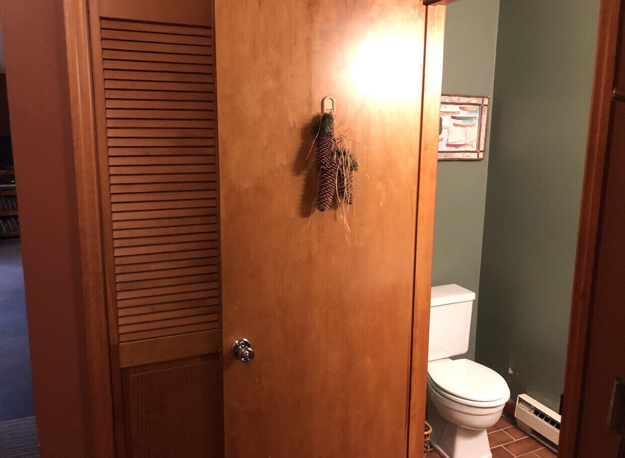 A wooden door with a latch, a small pine cone decoration, and a framed picture on the wall.