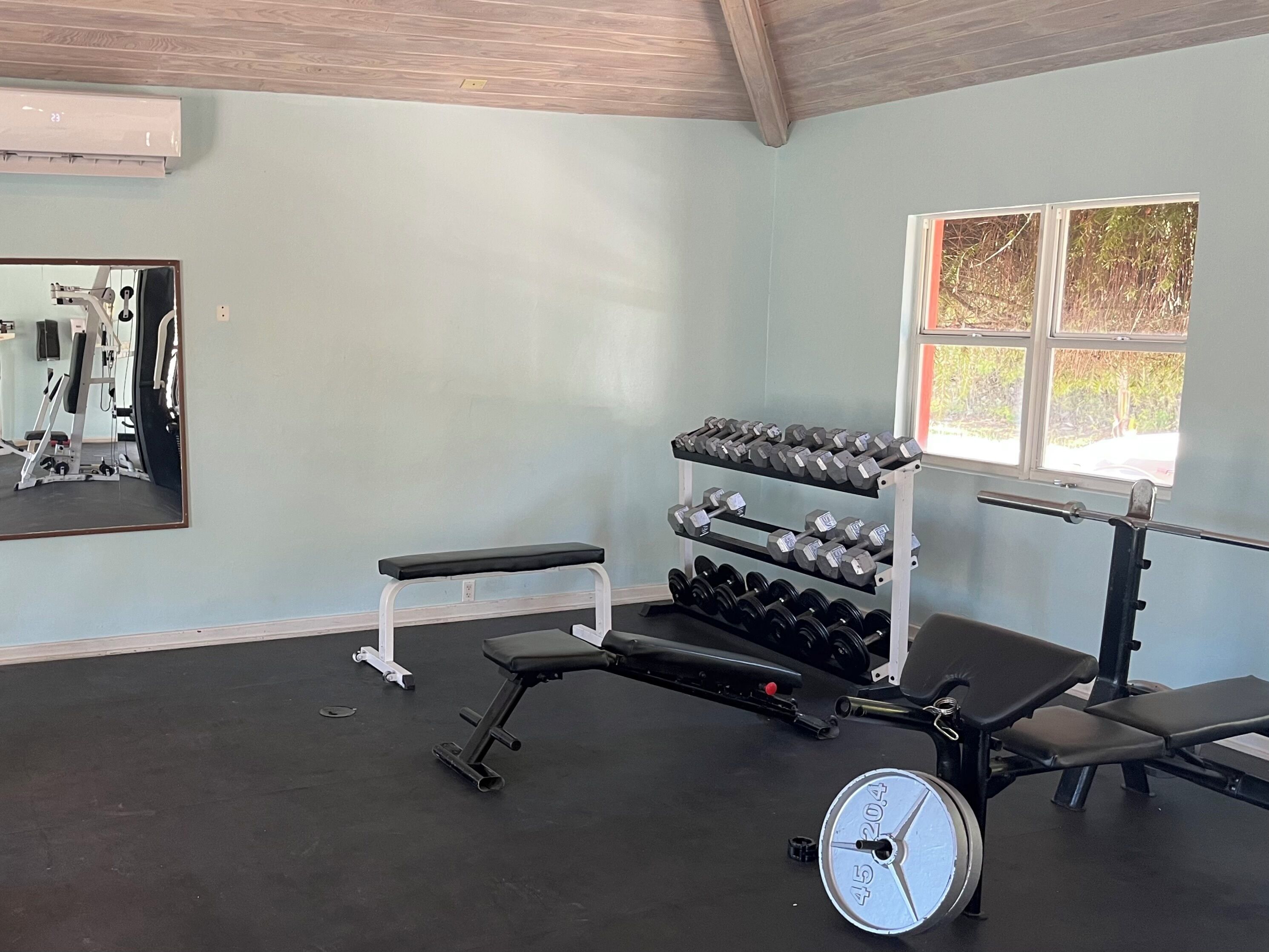 Une salle de sport équipée d’un banc, d’haltères, d’une balance et d’un miroir.