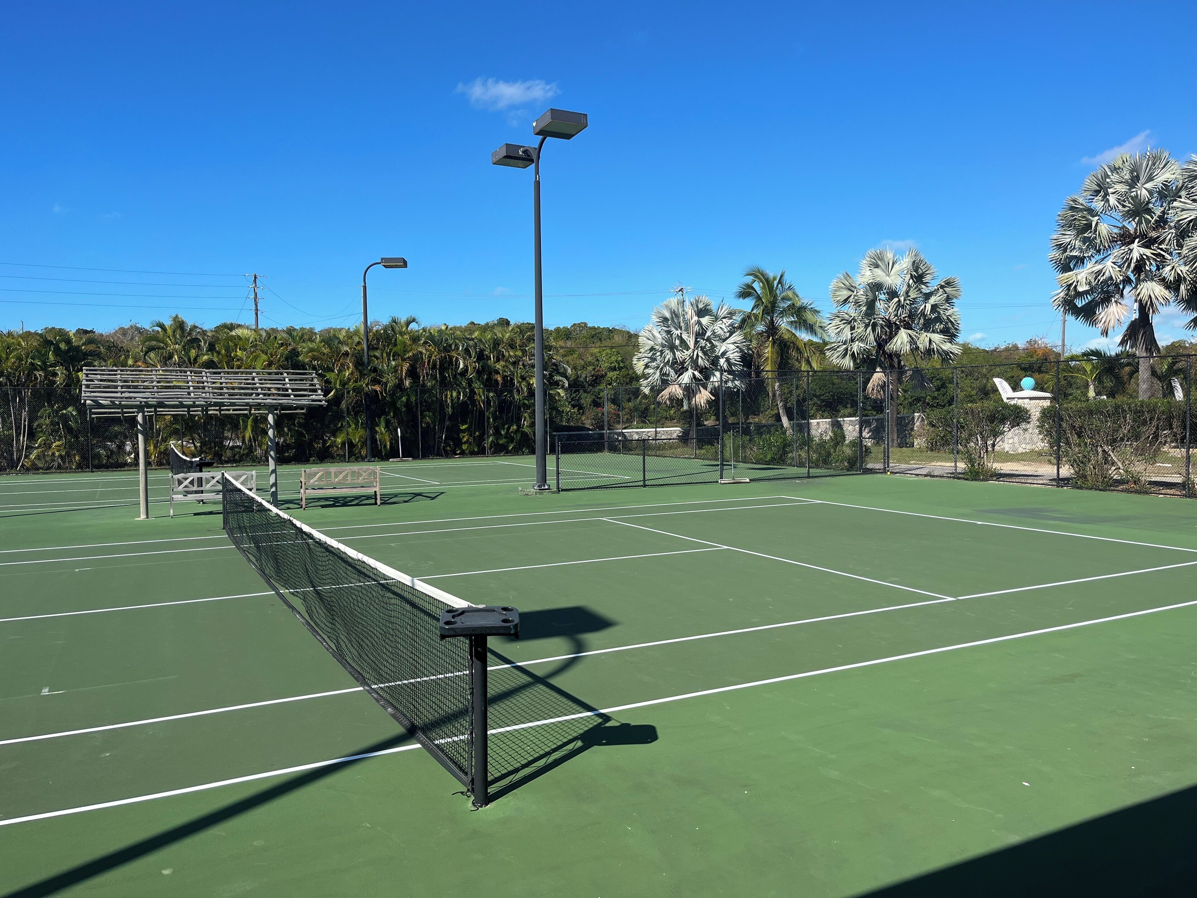A tennis court with a net, benches, and solar-powered lights.