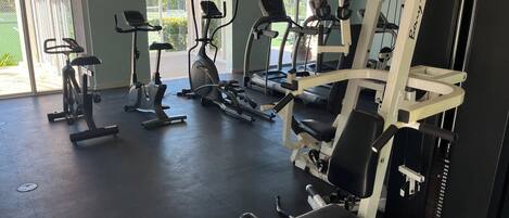 Une salle de sport équipée de divers appareils d’exercice, notamment des tapis de course, des vélos elliptiques et des appareils de musculation.