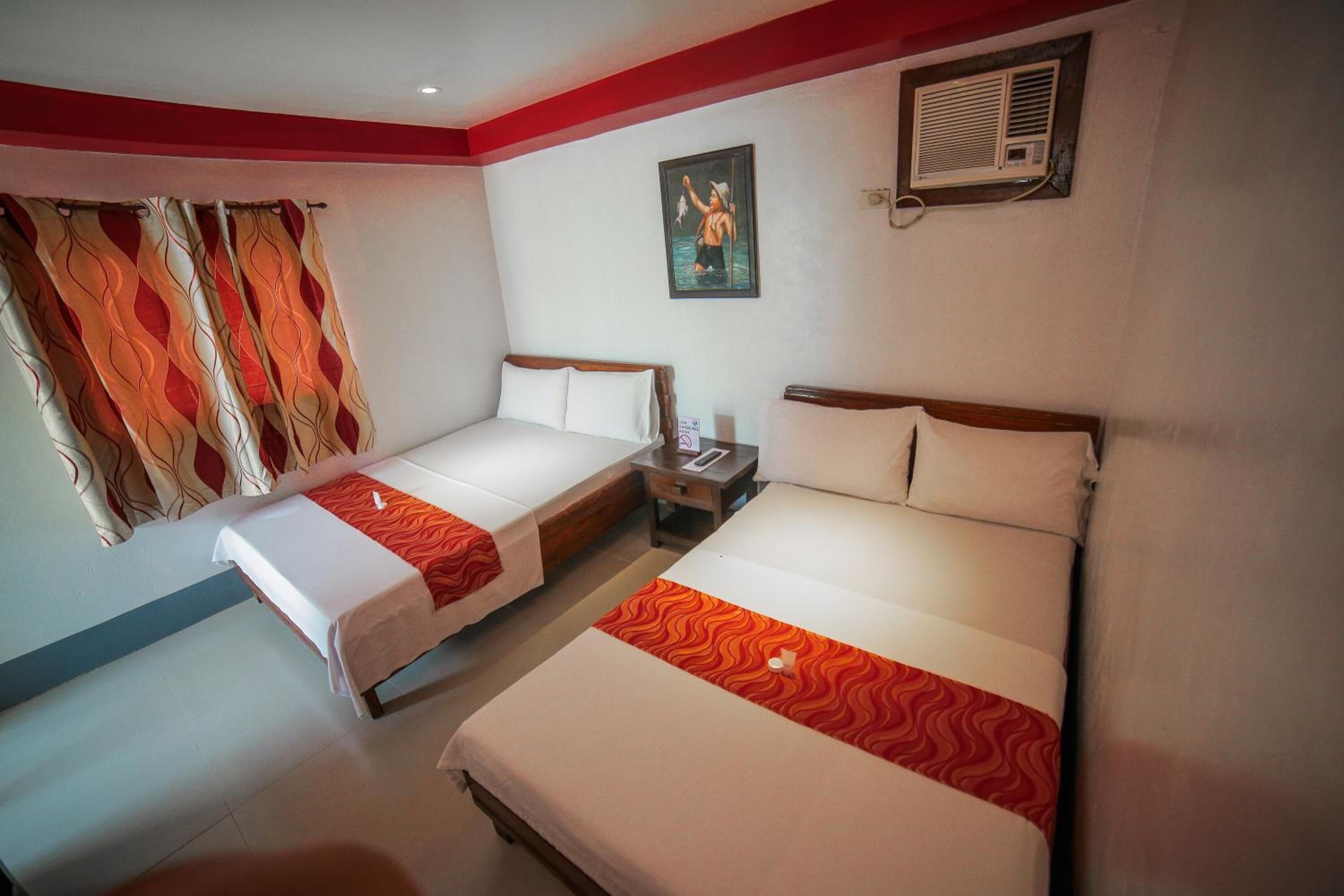 Une chambre d’hôtel avec deux lits simples, une table de chevet, un climatiseur fixé au mur et une fenêtre avec des rideaux à motifs.