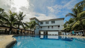 Une piscine au sol carrelé de bleu, entourée de palmiers et bordée d’un bâtiment doté de nombreuses fenêtres et de balcons.