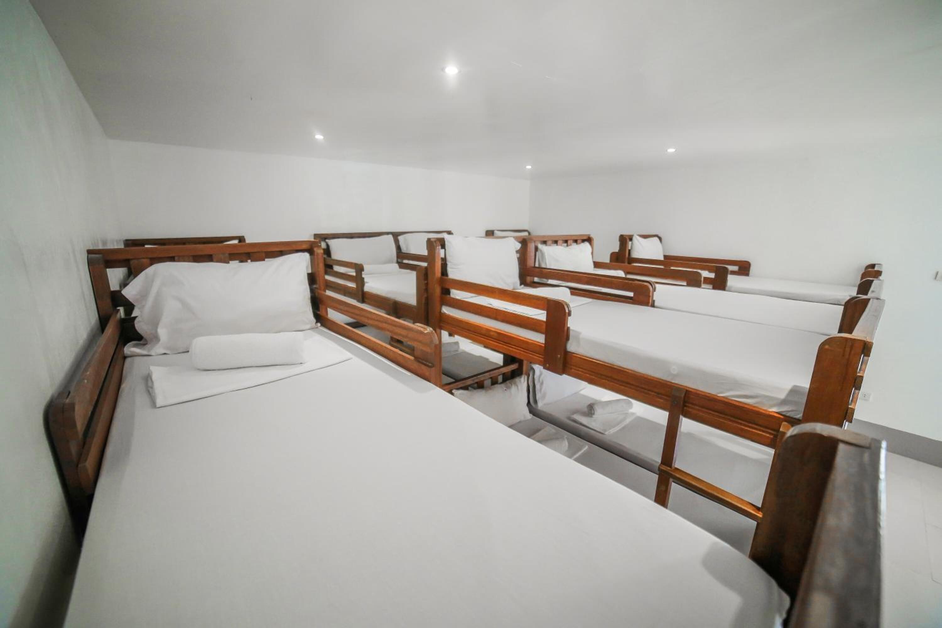 Ein Zimmer mit mehreren Holzkleinbetten, weißer Bettwäsche und einem schlichten, klaren Design.