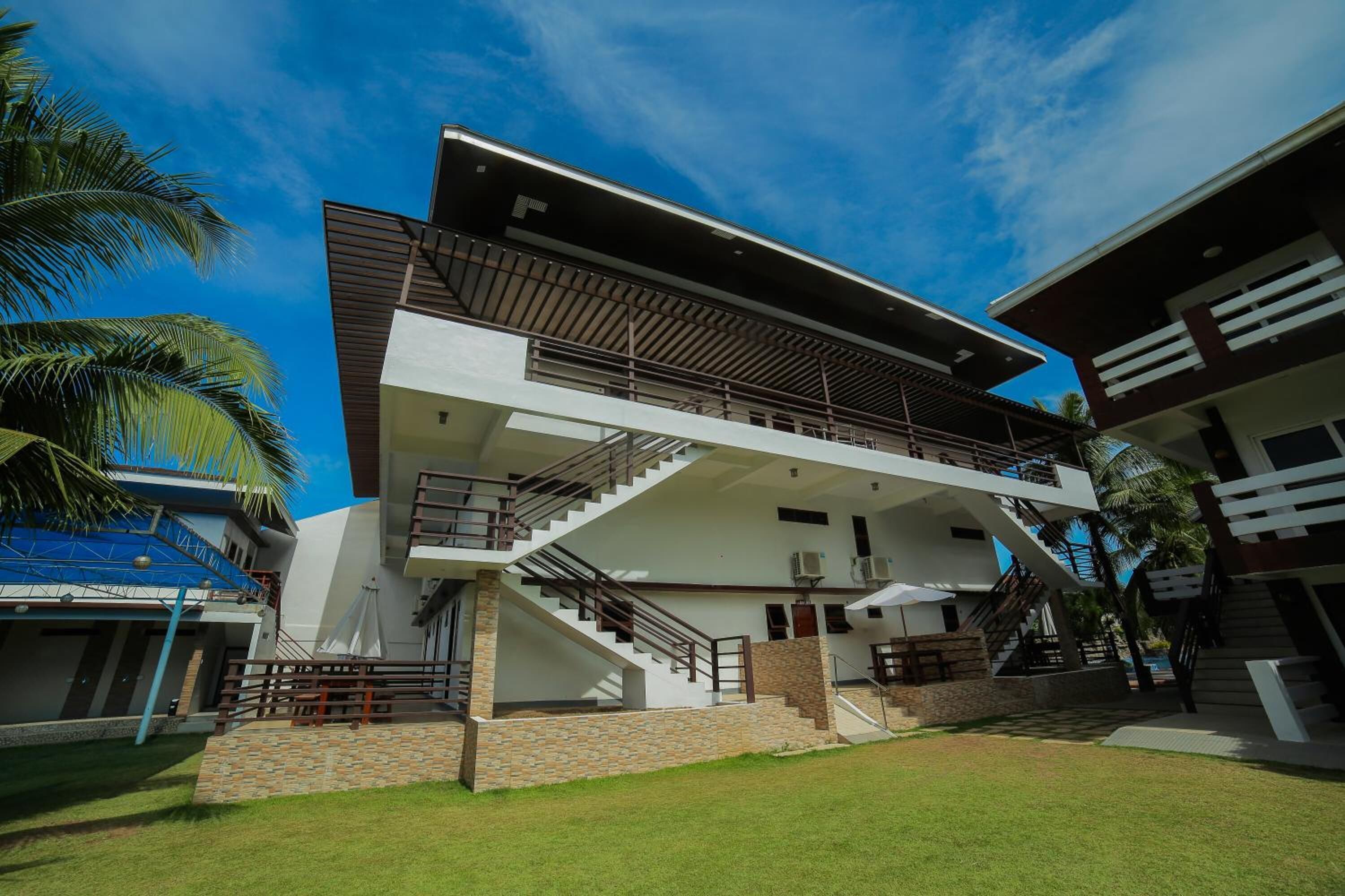 A modern multi-story building with a central staircase, balconies, and a well-maintained lawn.