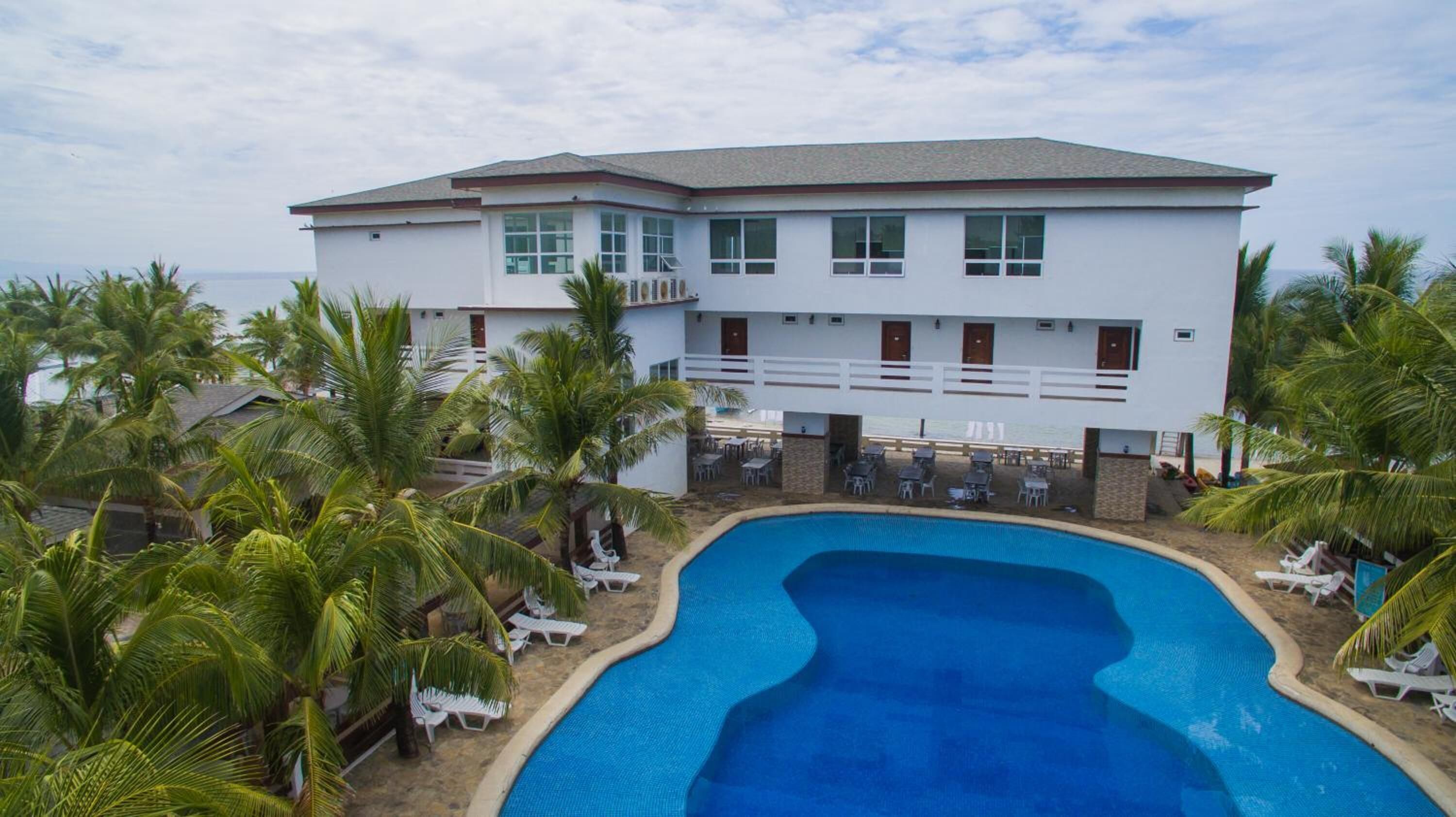 A hotel with a pool surrounded by palm trees and lounge chairs.