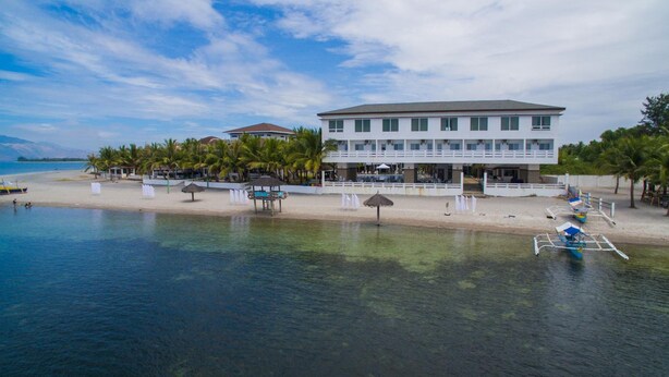 Un hôtel situé en bord de mer, doté d’une piscine, de parasols et de bateaux.
