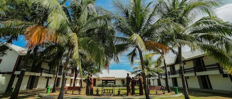 Un patio con palmeras, un pabellón y un edificio de fachada blanca y detalles oscuros.