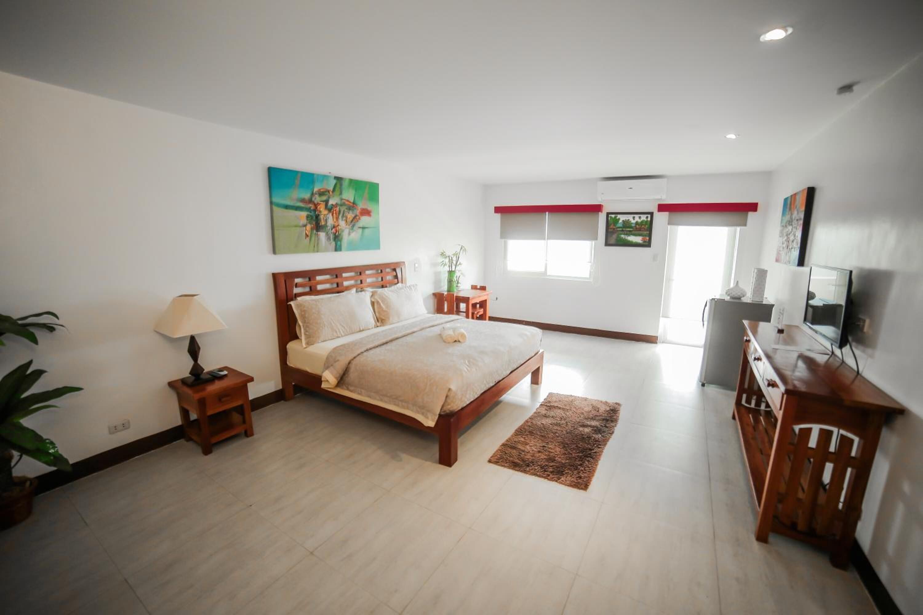 A bedroom with a bed, bedside table, lamp, and a TV on a wooden cabinet.