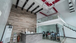 Un hall d’hôtel moderne avec un comptoir d’accueil, un escalier et un plafond haut orné d’un luminaire circulaire.