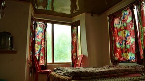 Un dormitorio con cama, una silla y una ventana con cortinas.