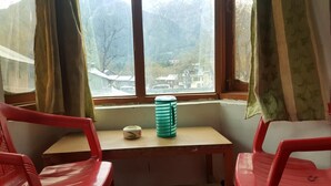 Una habitación con una pequeña mesa, dos sillas rojas, un ventanal con cortinas y vistas a edificios.