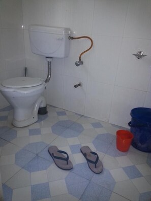 A bathroom with a toilet, a bidet, a showerhead, a red bucket, and a blue bucket on a tiled floor. - Rising Moon Guest House (Pokhara)
