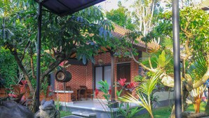 A brick house with a patio, surrounded by lush greenery and a small garden. - Pramewari Homestay (Ubud)