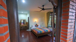 A bedroom with a bed, a ceiling fan, a nightstand, and a brick wall. - Pramewari Homestay (Ubud)