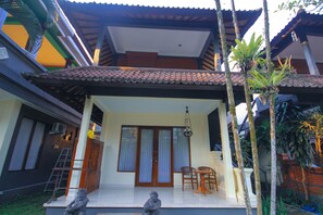 A house with a covered porch, a staircase, and a small garden with a statue. - Pramewari Homestay (Ubud)