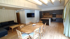 Un espacio habitable moderno con una mesa de comedor de madera, sillas, un sofá, televisión y una zona de cocina.