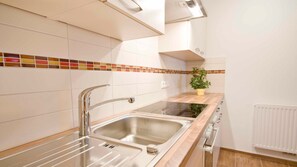 Una cocina con paredes de azulejos blancos, un lavamanos de acero inoxidable, un horno doble y una planta en maceta sobre la encimera.