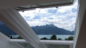 Un dormitorio con tragaluz, una cama con ropa de cama blanca y vistas a montañas y un lago.