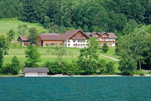 A large, multi-story building with a prominent central section and two smaller wings, surrounded by lush greenery and a body of water. - Apartment Brennerin - Haslbauer - family Resch (Haslach)