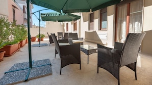 Un patio al aire libre con mobiliario de mimbre, una mesa de vidrio y sombrillas verdes.