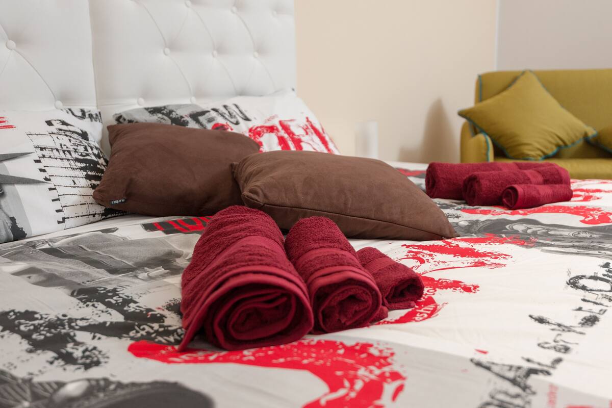 A neatly made bed with rolled towels, a tufted headboard, and patterned bedding.