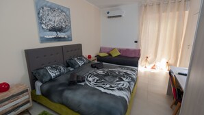 Un dormitorio con una cama grande, una mesita, una silla, una mesita de noche y un cuadro en la pared.