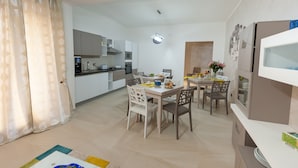 Una cocina moderna con armarios blancos, horno empotrado y microondas. Cuenta con un comedor con una mesa preparada para cuatro personas, rodeada de sillas.