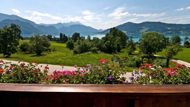 Une vue pittoresque d’un lac, avec des montagnes en arrière-plan, entouré d’une végétation luxuriante et de fleurs aux couleurs vives.