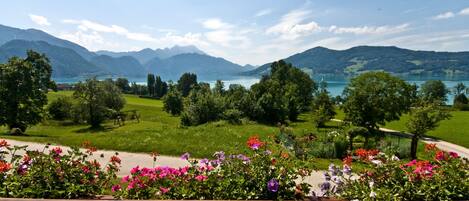 A scenic view of a lake with mountains in the background, surrounded by lush greenery and colorful flowers.