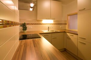 Una cocina moderna con mostradores de madera, estufa integrada, pileta y alacenas blancas.