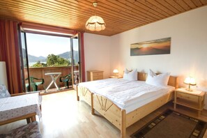 Un dormitorio con una cama grande, techo de madera, vista a través de un ventanal, una mesa con sillas y un cuadro en la pared.