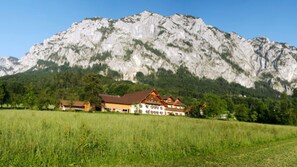 Un refugio de montaña con una imponente vista de montañas al fondo, un campo cubierto de hierba en primer plano y un cielo despejado.