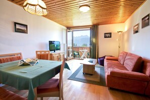 Una habitación con una mesa de comedor, un sofá, un televisor y vistas a las montañas a través de un ventanal grande.