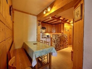 Ein gemütlicher Essbereich aus Holz mit Tisch und Stühlen, eine Küche im Hintergrund und ein Kamin aus Stein.