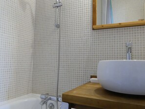 Une salle de bain avec une baignoire blanche, un meuble-lavabo en bois et un mur carrelé.