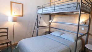 Une chambre avec un lit superposé, un bureau et une chaise, un tableau encadré au mur et une lampe.