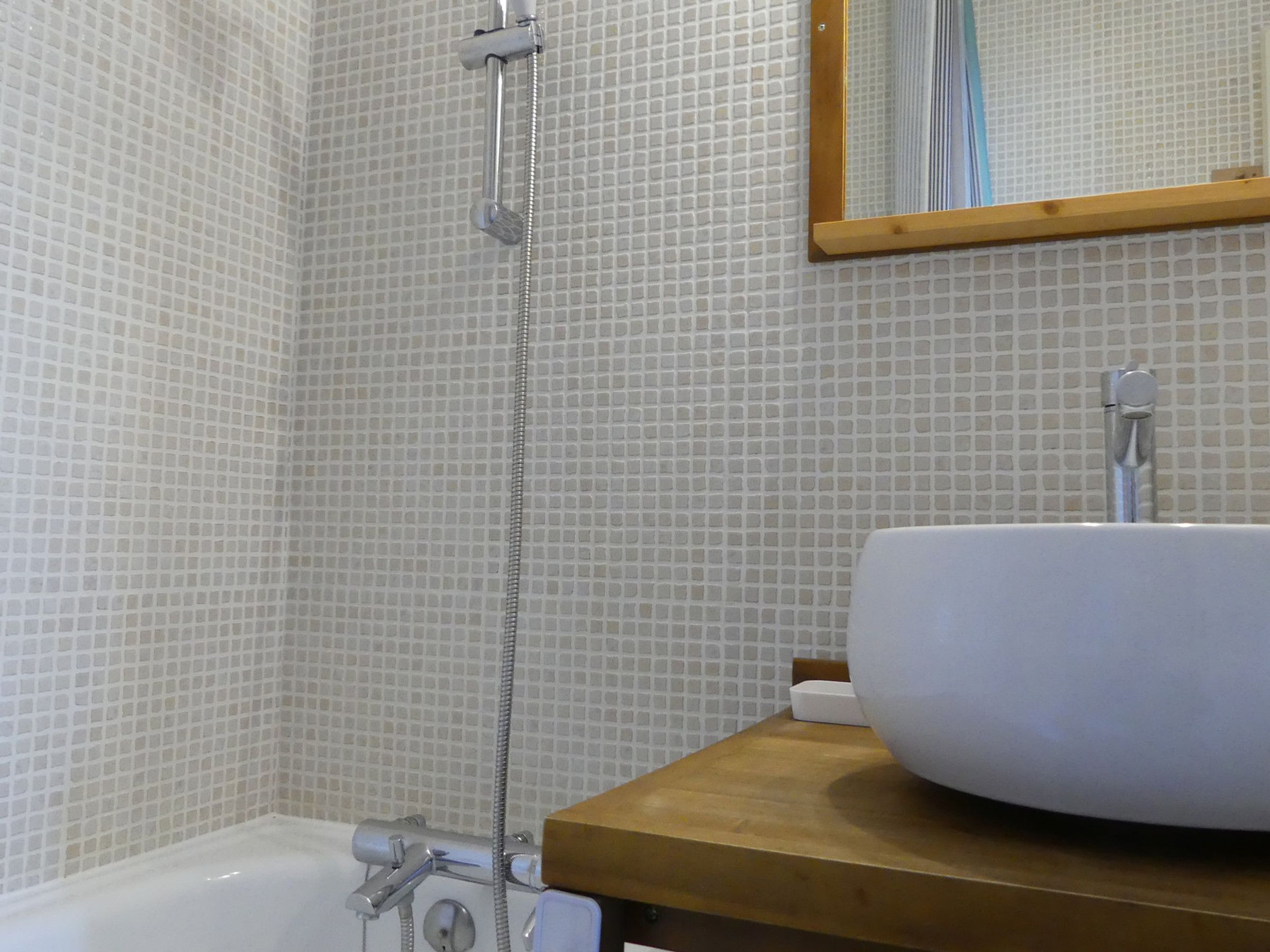 A bathroom with a white bathtub, a wooden vanity, and a tiled wall.
