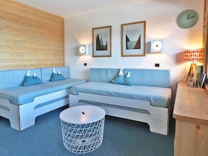 A cozy room with a wooden wall, two blue sofas with mountain-shaped pillows, a round white table, and two wall-mounted picture frames.